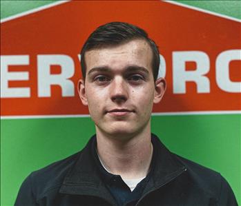 Male employee with dark blonde hair smiling in front of SERVPRO logo